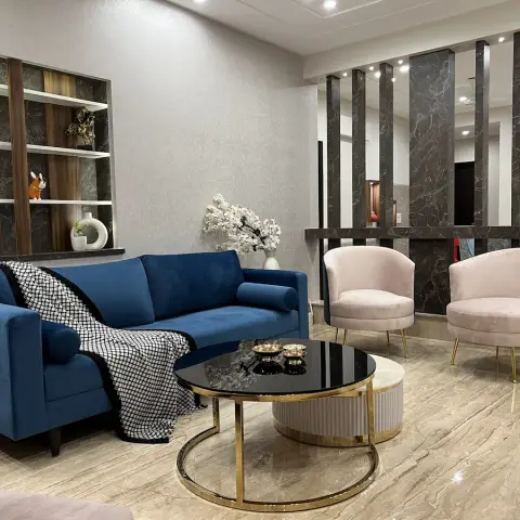 Sapphire velvet sofa and two blush tub chairs on gold legs face a dark-marble fin screen that separates the living zone from the dining