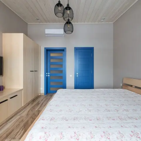 Scandinavian bedroom with a light birch wardrobe and TV console, exposed wood-plank ceiling, and twin cobalt-blue doors.