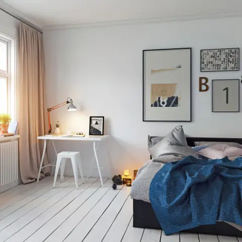 Scandinavian bedroom with whitewashed plank flooring, a small white trestle desk and a gallery wall of graphic prints beside the bed.