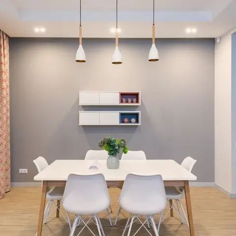 Scandinavian dining nook with three cone pendant lights over a white table, patterned rust curtains, and floating two-tone display cabinets on a grey wall.