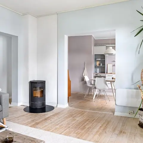 Scandinavian living room with a freestanding wood-burning stove and an open doorway to a dining nook beyond