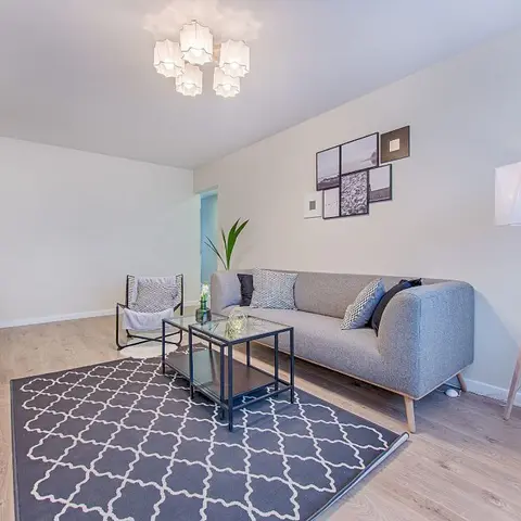 Scandinavian living room with a grey fabric sofa, a black-and-white trellis-pattern rug, a gallery wall of framed prints, and a geometric tripod floor lamp.