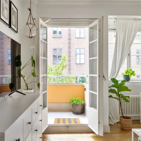 Scandinavian living room with a white TV console under a gallery wall of framed photos, French doors open to a small balcony