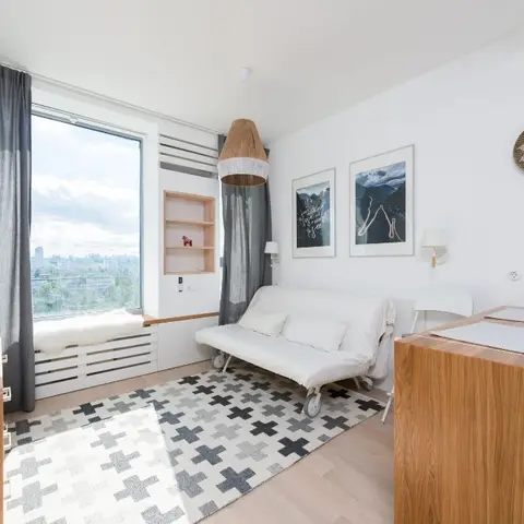 Scandinavian-style living nook with a woven rattan pendant, grey curtains, a graphic cross-pattern rug, and a built-in window seat overlooking the city