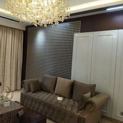 Show-flat living room: two deep-buttoned taupe velvet sofas carrying 'Do not sit' placards, facing a mirror-backed square lattice screen in a dark wood frame