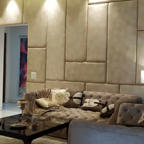 Show-flat living room where a wall of staggered beige leatherette upholstered blocks meets a marble-clad TV panel with a floating wenge console