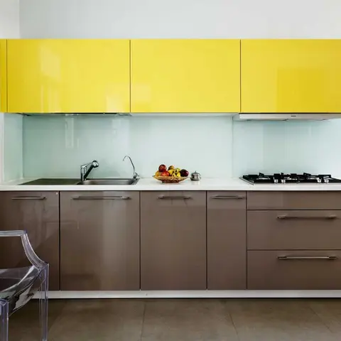 Single-wall kitchen with glossy yellow upper cabinets, brown gloss base units and a clear ghost chair in the corner