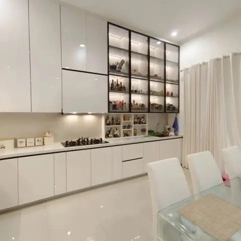 Single-wall white gloss handleless kitchen running the length of the room into a black-framed glass display cabinet stacked with curios and lit shelf by shelf
