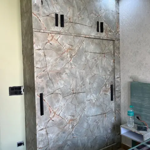 Site shot of a full-height sliding wardrobe with loft shutters wrapped in grey-and-rust marble-print laminate and slim black bar handles