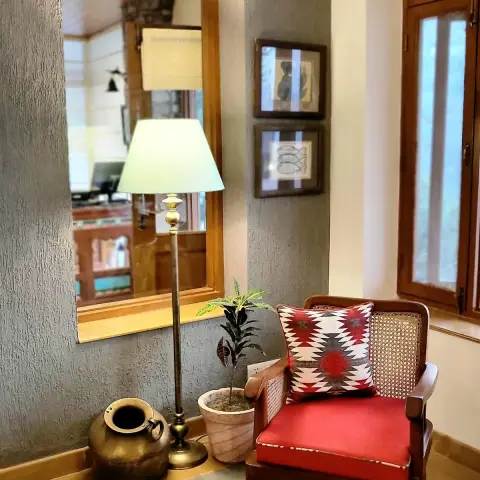 Sitting corner against a grey textured plaster wall — teak-framed mirror recessed above a ledge holding a brass pot and a brass floor lamp
