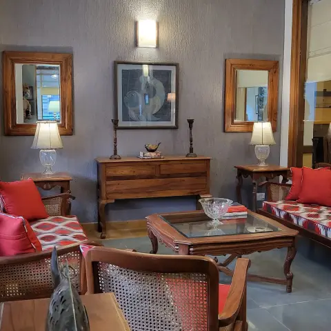 Sitting room against a coarse grey textured wall, a pair of teak-framed mirrors flanking a framed fish painting over a teak chest