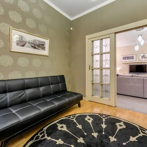 Sitting room with a black leather bench sofa against botanical-print wallpaper, a round medallion rug, and a glazed sliding door to the living room.