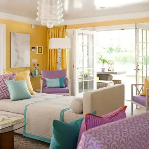 Sitting room with mustard yellow walls, a cushioned daybed in teal-trimmed white, purple armchairs, and French doors opening to a patio.