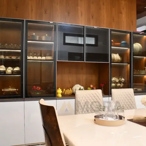 Six-bay glass-fronted crockery unit lit shelf by shelf, filled with steel cookware, teacups and painted china