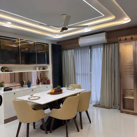 Six beige channel-stitched chairs round a white sintered-stone dining table, with a rose-gold framed smoked-glass crockery unit over a mirrored curio niche