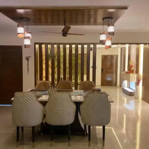 Six-seat marble-top dining table with quilted cream and tan chairs under a wood-clad ceiling raft and two clusters of cylindrical pendants