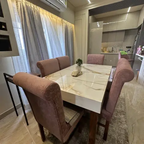 Six-seater Calacatta-look stone dining table with dusty-pink rolled-back velvet chairs on a faded grey rug