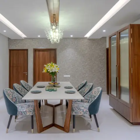 Six-seater dining with a white stone-top table on a walnut V-leg base, teal velvet and printed-fabric chairs