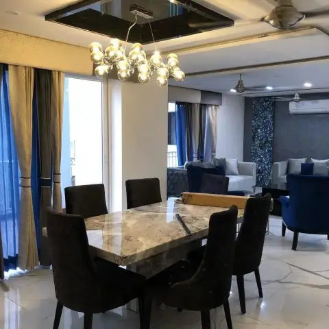 Six-seater marble-top dining table with dark quilted high-back chairs under a brass multi-globe cluster pendant hung from a tinted-mirror ceiling recess