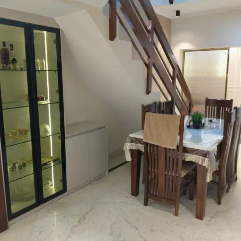 Six-seater teak dining set tucked under the timber staircase, still under its plastic-covered lace cloth