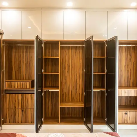 Six-shutter wardrobe photographed with its doors swung open to show teak-veneer interiors, a pull-out trouser rack
