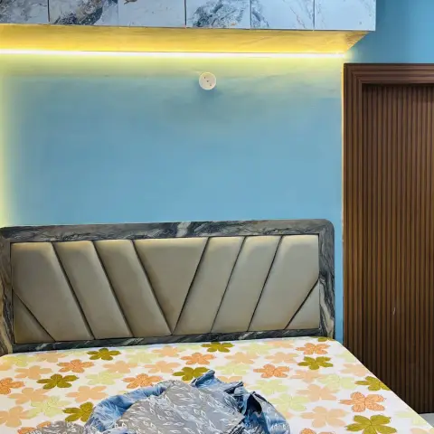 Sky-blue bed-back niche outlined by a warm LED strip, holding a chevron-tufted beige headboard framed in grey marble-look edging