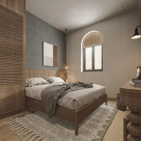 Slatted-wood bed under an arched window with wooden venetian blinds, facing a full-height louvred oak wardrobe, with a woven fringed rug over plank flooring