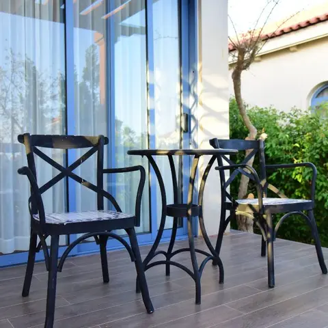 Small balcony seating nook with two black cross-back bistro chairs and a round metal table beside sheer-curtained sliding doors