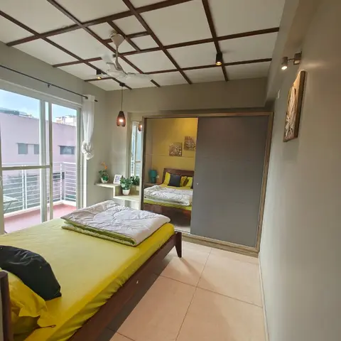 Small bedroom with a mustard-yellow bedspread, a mirrored sliding wardrobe, and a diamond-grid wood-trimmed false ceiling.