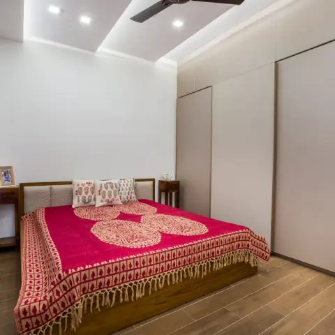Small bedroom with a teak bed under a magenta block-printed bedspread with tasselled edges, matching teak side tables either side