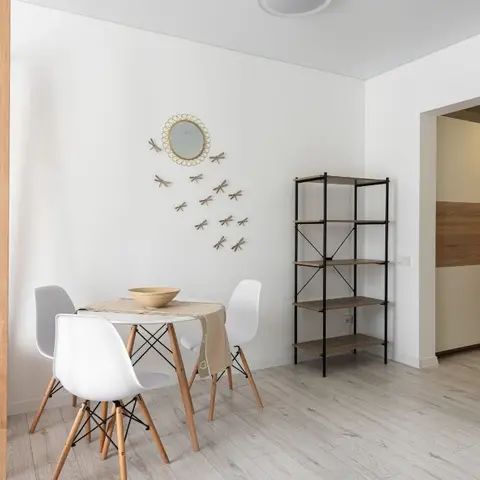 Small dining nook with a round white table, wood-legged Eiffel chairs and a dragonfly wall-art arrangement around a mirror