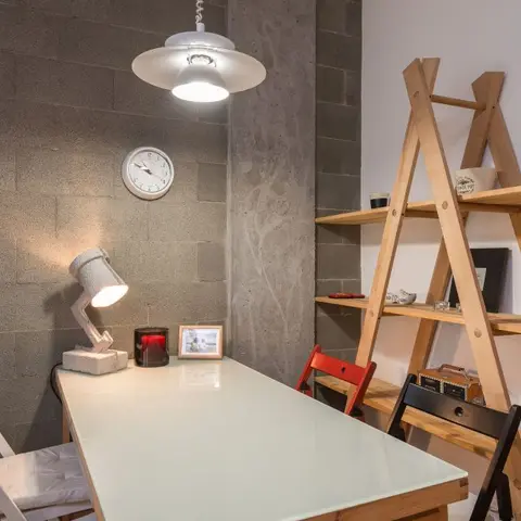 Small dining nook with an exposed concrete-block wall, a glass-top table surrounded by mismatched red, black and white folding chairs