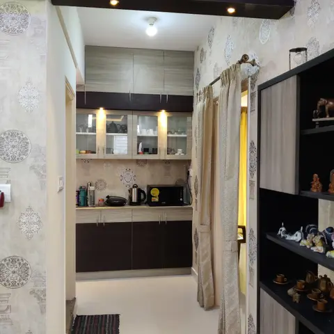 Small kitchenette viewed through an ornate mandala-patterned wallpapered passage, with glass-front upper cabinets and a curio display shelf nearby.
