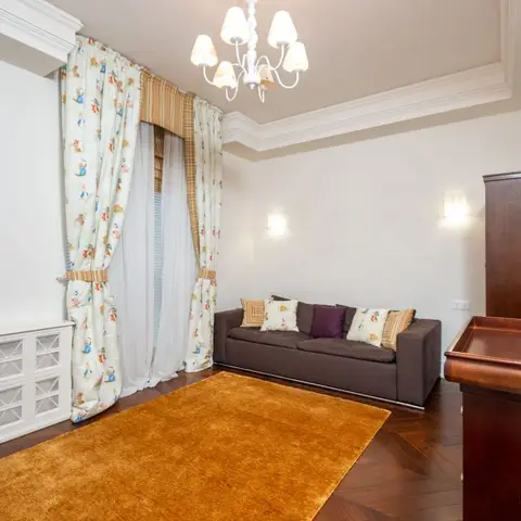 Small sitting room with a brown sofa on a mustard rug, novelty-print floor-length curtains and a dark wood armoire in the corner