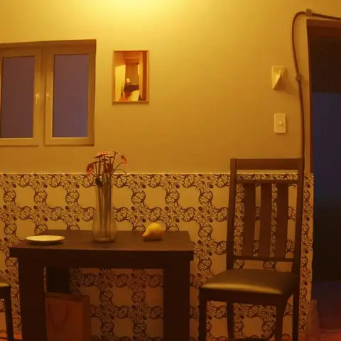 Small two-chair dining nook against a patterned tile wainscot wall, with a refrigerator to one side under warm ambient lighting.
