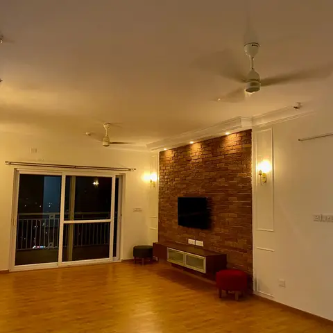 Sparsely furnished living room with an exposed red-brick TV feature wall lit by recessed spotlights, a floating wood console below