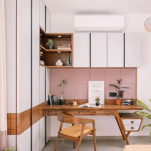 Study corner in a bedroom with a mid-century wood desk and chair against a dusty-pink upholstered panel wall