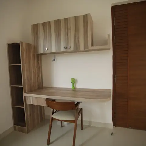 Study corner with a wall-mounted wood-laminate desk, open shelving and an overhead loft cabinet