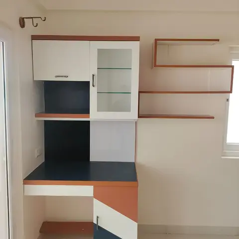 Study desk unit with a glass-shelf display cabinet above, floating shelves to the side, and a color-blocked navy, white and rust laminate finish