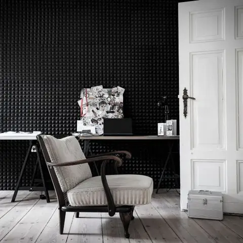 Study nook with a black pyramid-textured acoustic wall behind a trestle desk, a vintage bentwood armchair, and a mood board of magazine clippings.