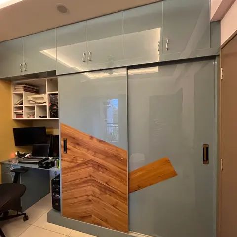 Study nook with a built-in desk and open shelving beneath a glossy grey sliding-door wardrobe featuring a geometric wood-panel accent.