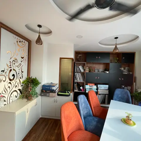 Study nook with a carved wood jaali screen partition, an oval cove-lit ceiling, a wall of black-and-wood bookshelves, and orange and blue accent chairs.