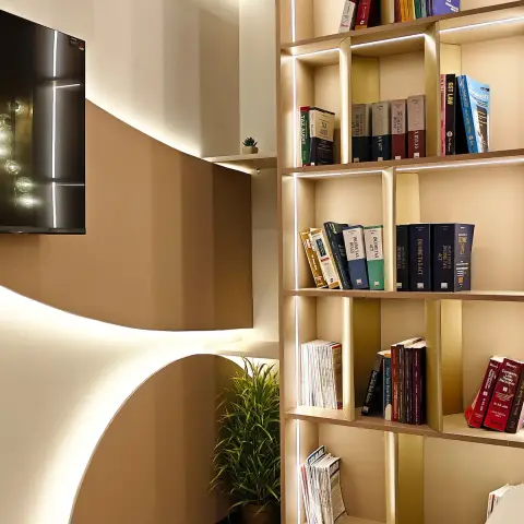 Study nook with a curved plaster feature wall, a wall-mounted TV, and a backlit open bookshelf display.