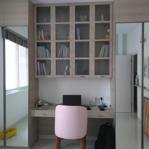 Study nook with a glass-front bookshelf above a built-in desk with a pink stool, flanked by full-height mirrored wardrobes.