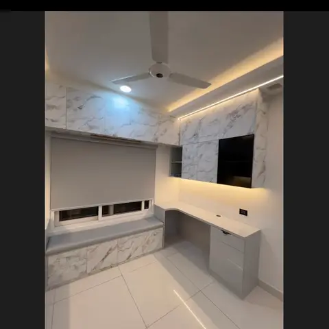 Study nook with a marble-clad wall, a built-in L-shaped white desk, a wall-mounted TV niche, and an upholstered window seat with a marble base.