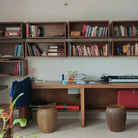 Study nook with a row of wall-mounted open wood cubby bookshelves above a long floating study desk holding a keyboard and books.