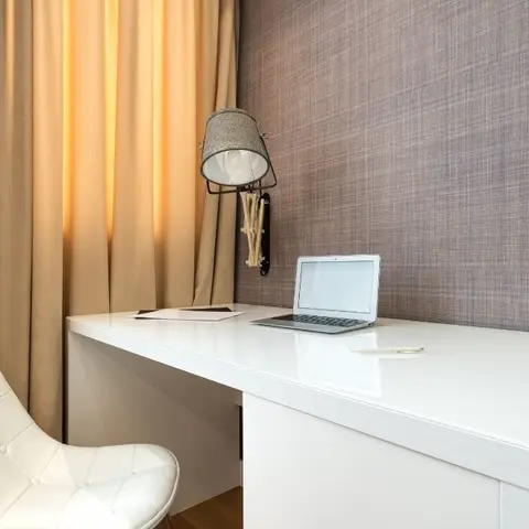 Study nook with a white gloss desk, a tufted white leather chair and an industrial wall-mounted lamp against a textured woven wallcovering