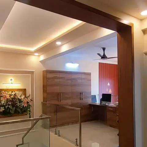 Study seen through a teak-framed opening from the glass-balustraded stair landing: a walnut storage wall and an L-shaped desk with two monitors set against a