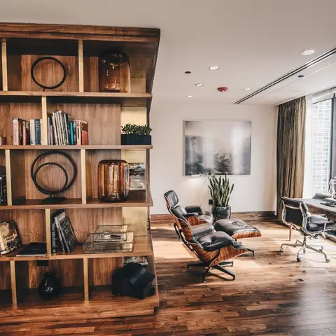 Study with a wood-and-brass library shelving wall, a leather Eames lounge chair and ottoman