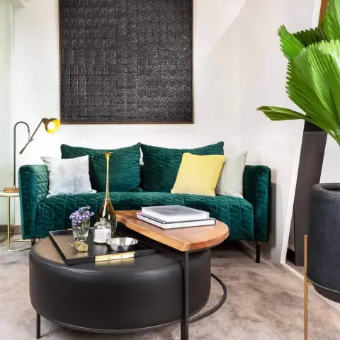 Styled living corner with an emerald quilted velvet sofa under a large black cast-relief panel, a single yellow knit cushion breaking up the greens
